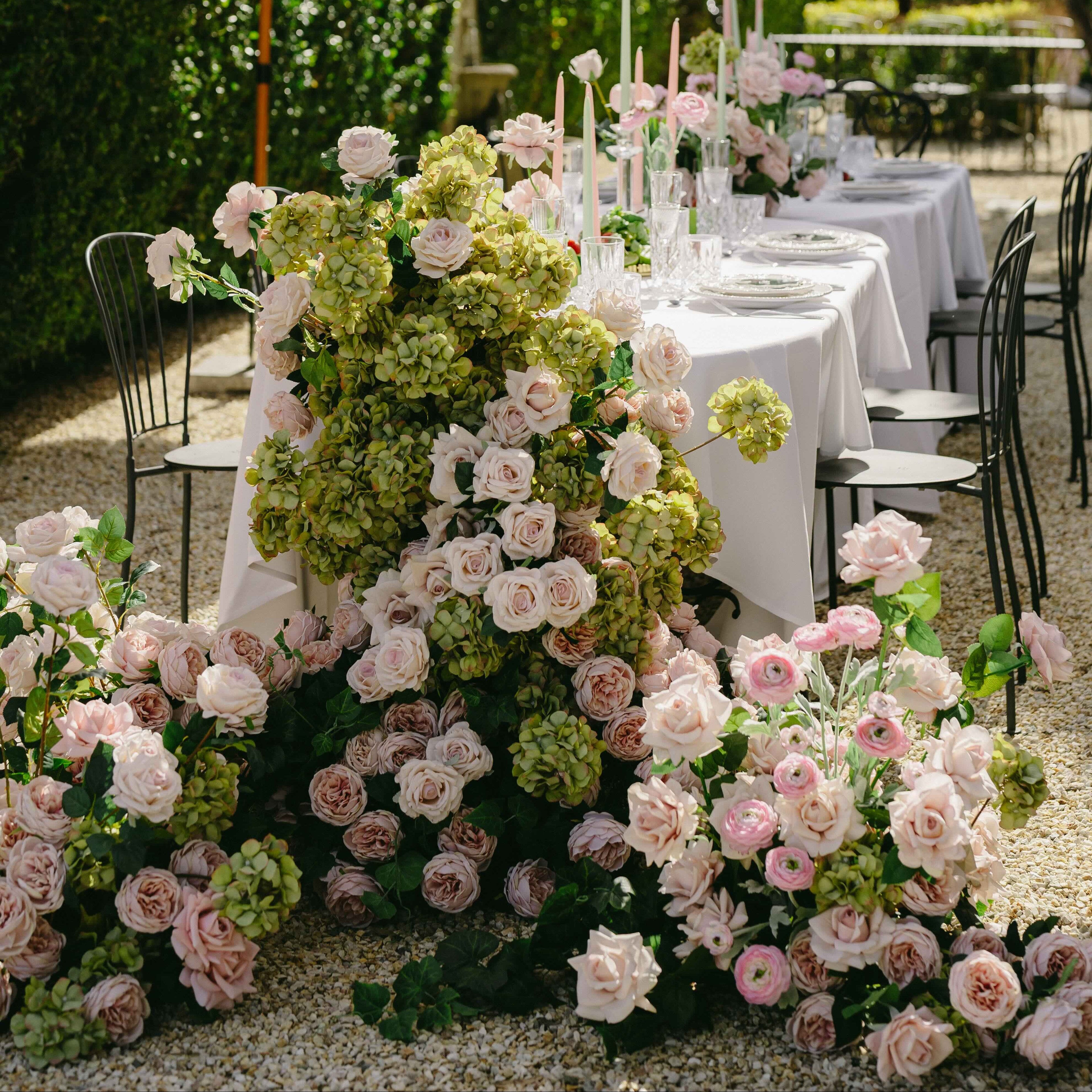 Outdoor wedding setup with floral arrangements and tables in a garden setting.